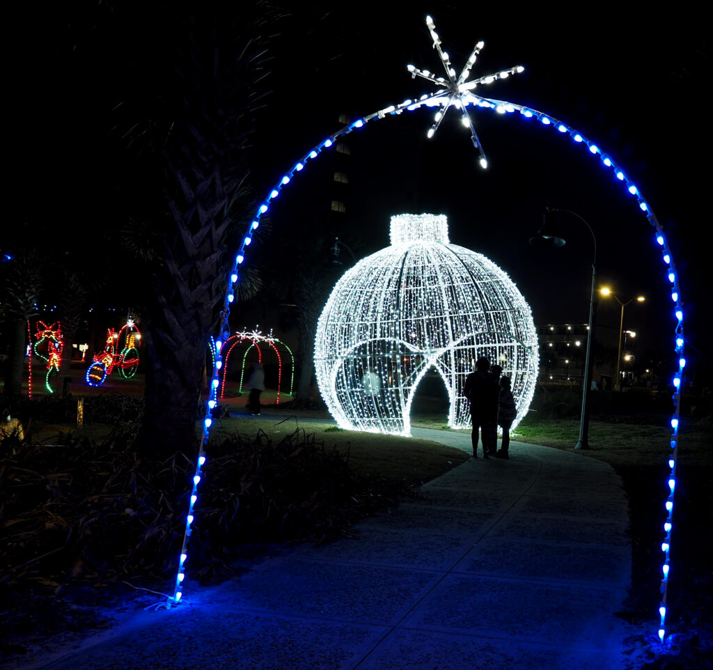 A family stopping under a giant illuminated ornament framed by a blue light archway over the walkway.